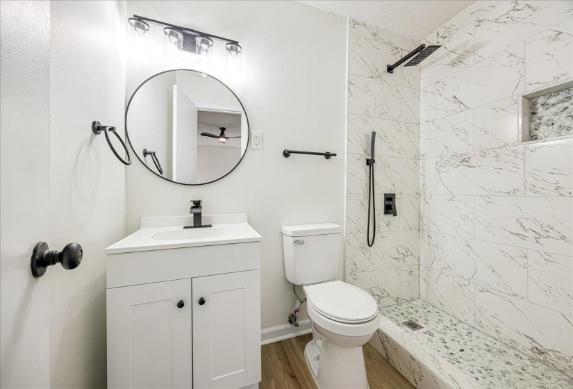 Full bath with a marble finish shower, vanity, and dark wood-type flooring