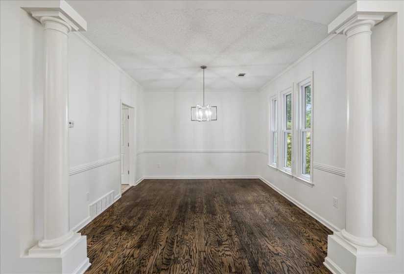 Spacious interior room featuring dark wood-finish flooring, white walls with wainscoting, crown molding, and a contemporary chandelier