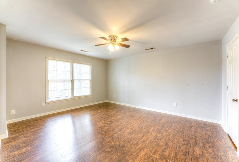 Spacious room featuring wood-finish flooring, light grey walls, and a ceiling fan with integrated lighting