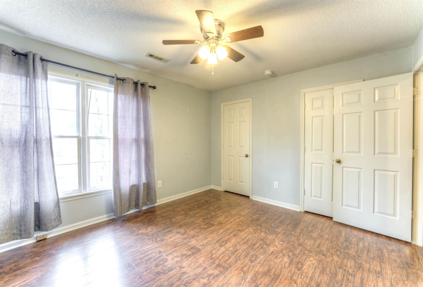 Spacious room with wood-finish flooring, light-colored walls, and a ceiling fan with light fixture