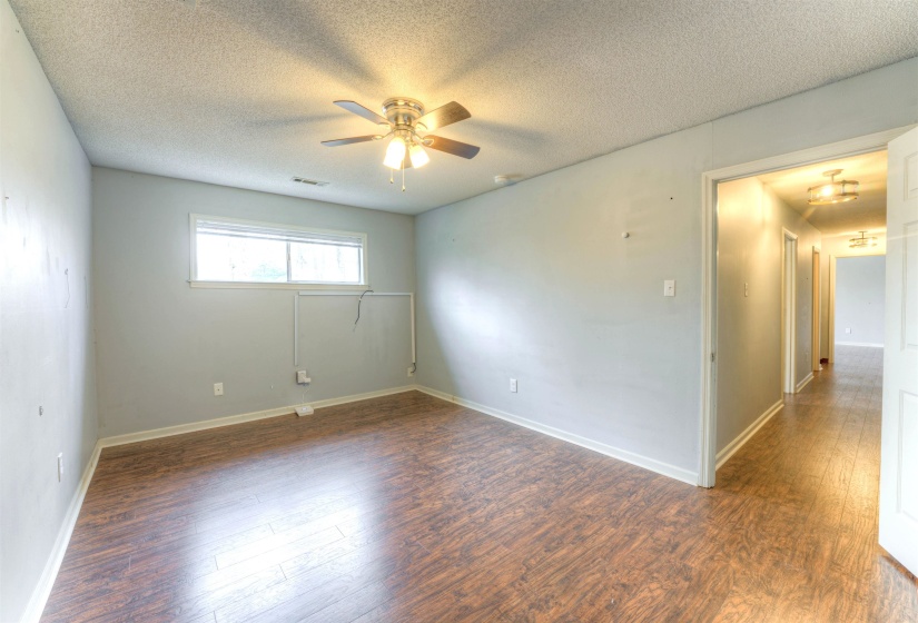 Spacious room featuring wood-finish flooring, light gray walls, a ceiling fan with integrated lighting, and a window for natural illumination
