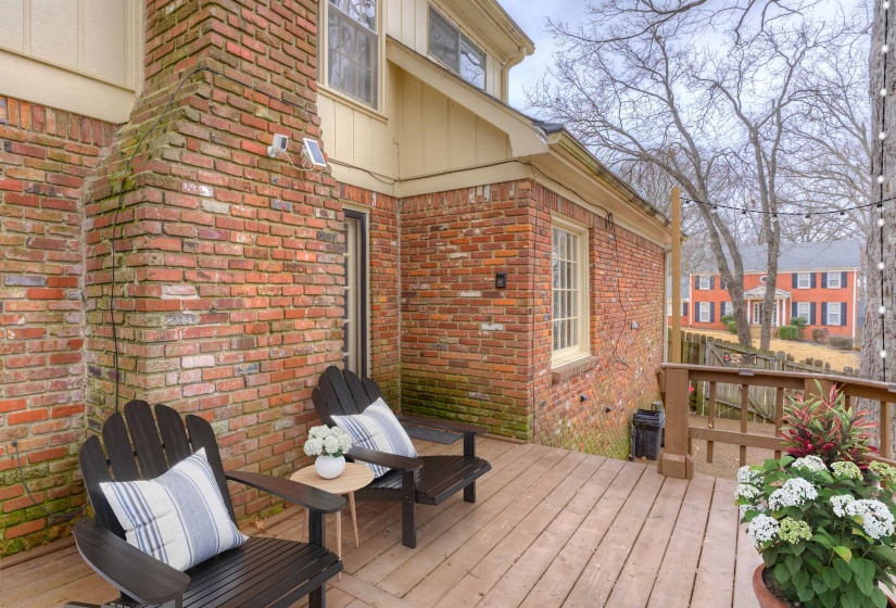 Exterior wood-finish deck with a wood railing, surrounded by a brick façade and a prominent brick chimney