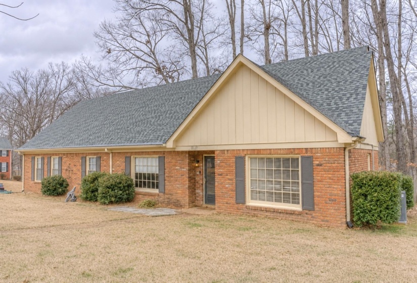 Brick exterior featuring a gray shingle roof, light-colored siding on the gable, dark shutters, and mature landscaping