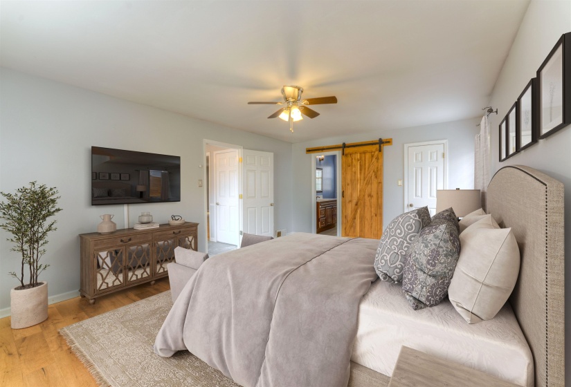 Bedroom featuring light wood-finish flooring, a ceiling fan with integrated lighting, a natural wood barn door, and a built-in entertainment console