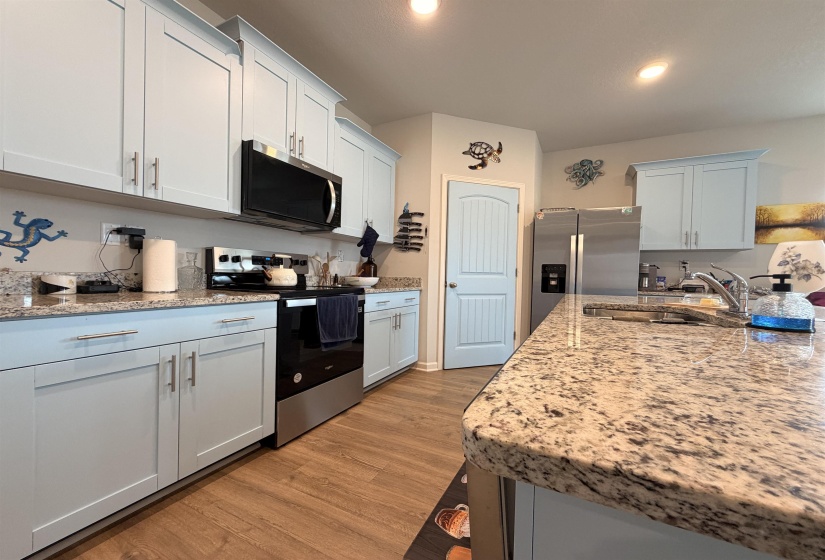Kitchen with granite countertops, light-toned cabinetry, stainless steel appliances, and wood-finish flooring
