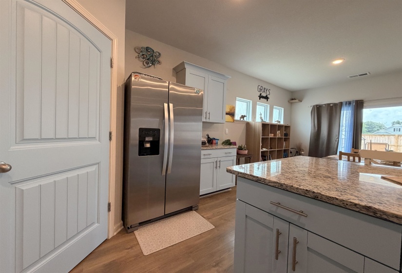 Spacious kitchen featuring an expansive island with a granite countertop, light-toned cabinetry with contemporary hardware, wood-finish flooring, and a stainless steel side-by-side refrigerator