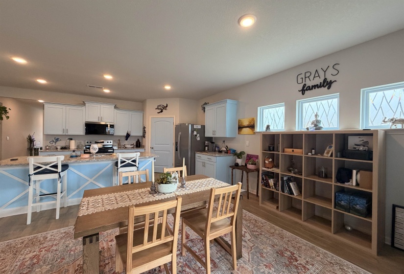 Open-concept kitchen featuring light-toned cabinetry, stainless steel appliances, and a central island with a light blue base and solid surface countertop