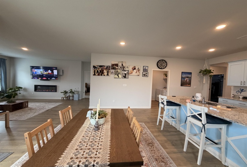Open-concept living area featuring wood-finish flooring, recessed lighting, a built-in electric fireplace, and a kitchen island with a granite-style countertop and light blue base
