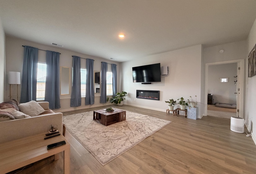 Living area featuring wood-finish flooring, an electric fireplace insert, and multiple windows with blinds
