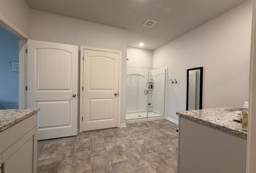 Spacious bathroom featuring a glass-enclosed shower, dual vanity countertops with granite-style surfaces, and wood-finish flooring