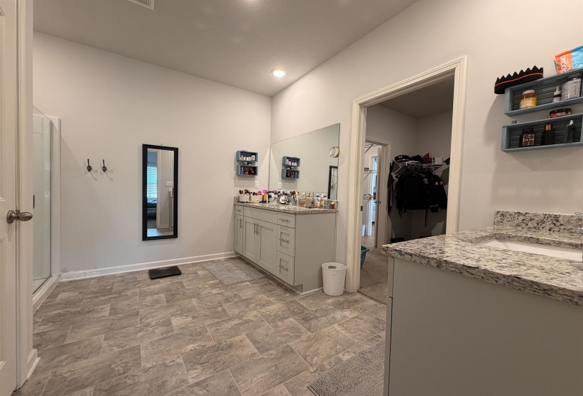 Spacious bathroom featuring dual vanities with light-colored countertops, a large wall-mounted mirror, recessed lighting, and rectangular tile flooring