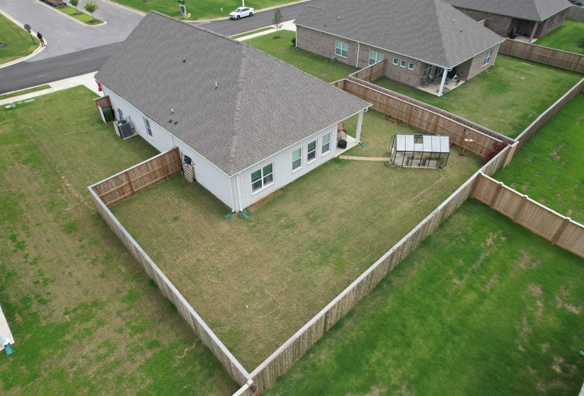 Expansive fenced backyard featuring a covered patio, a detached greenhouse, and green lawn space