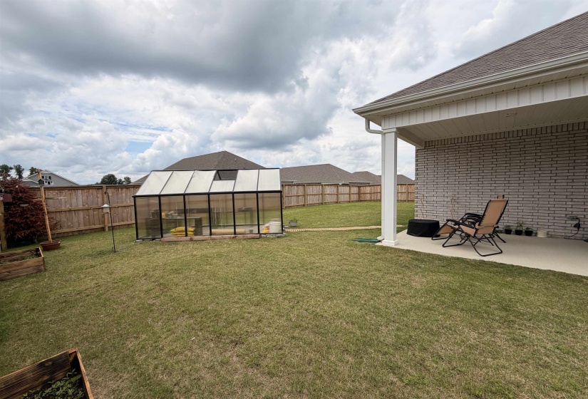 Expansive backyard featuring a large greenhouse, privacy fencing, and a covered concrete patio