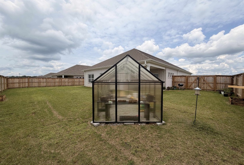 Spacious backyard featuring a modern greenhouse structure, privacy fencing, and a manicured lawn