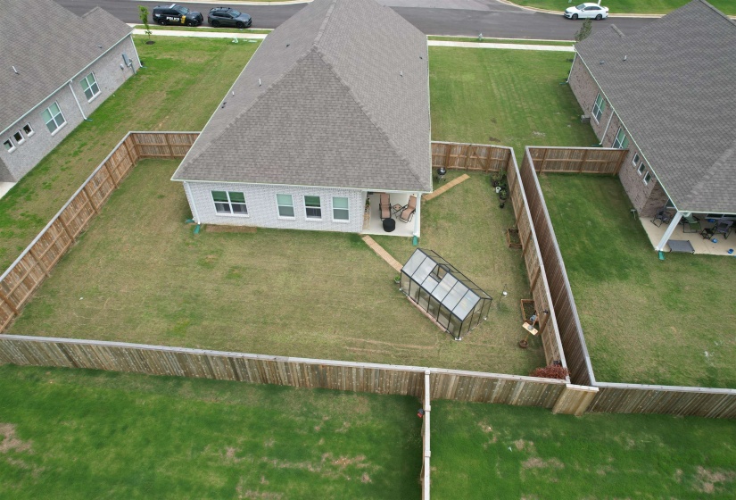 Fenced backyard featuring a rear patio, greenhouse, and level lawn