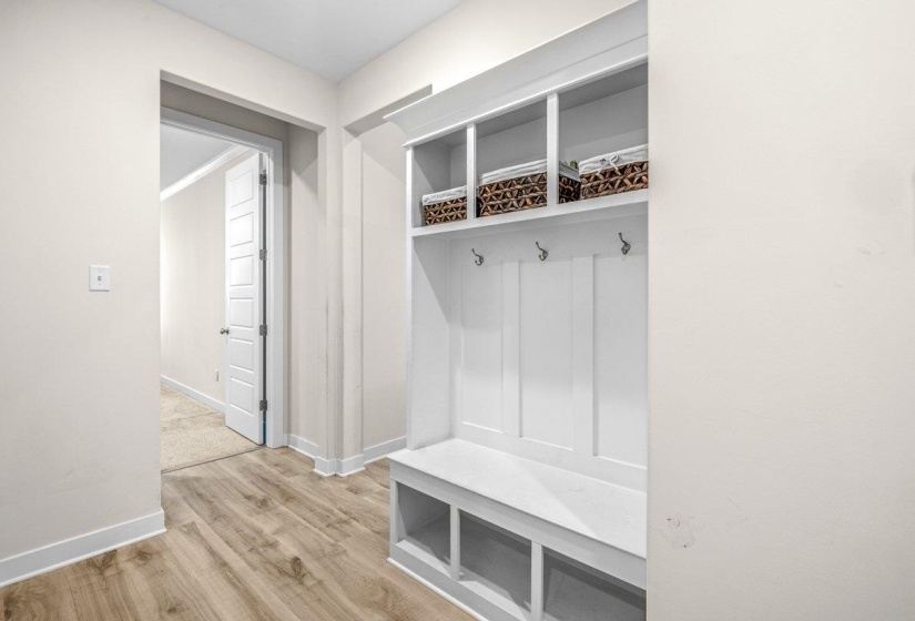 Entryway featuring wood-finish flooring, a built-in white mudroom bench with cubbies and upper shelving, paneling, and three coat hooks