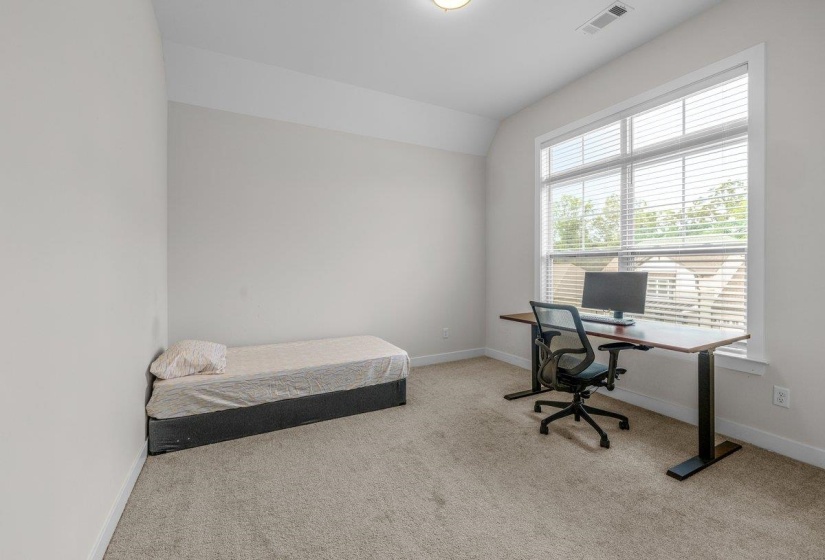 Carpeted room with a large window featuring blinds, a built-in recessed ceiling light, and a ceiling ventilation register