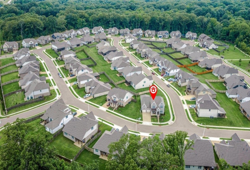 Aerial view of a residential development featuring uniform-style homes with grey shingle roofs and fenced backyards, situated on curved asphalt streets with paved sidewalks