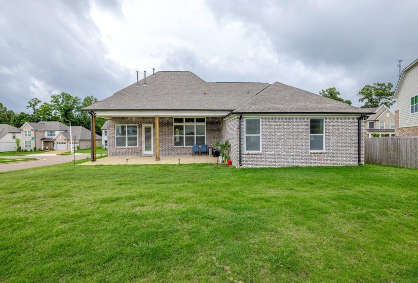 Expansive backyard featuring a large green lawn, a covered patio, and a brick exterior with multiple windows