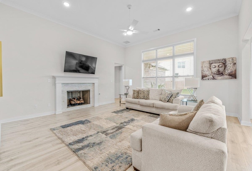 Spacious living area featuring a fireplace with a white mantel and tile surround, wood-finish flooring, a ceiling fan, recessed lighting, and large windows