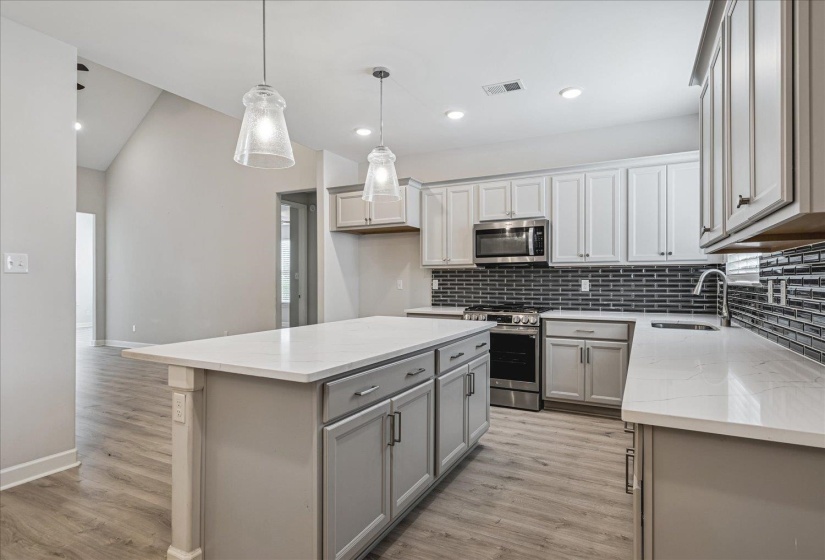Kitchen featuring an island with quartz countertop, light gray cabinetry, stainless steel appliances, a dark tile backsplash, and wood-finish flooring
