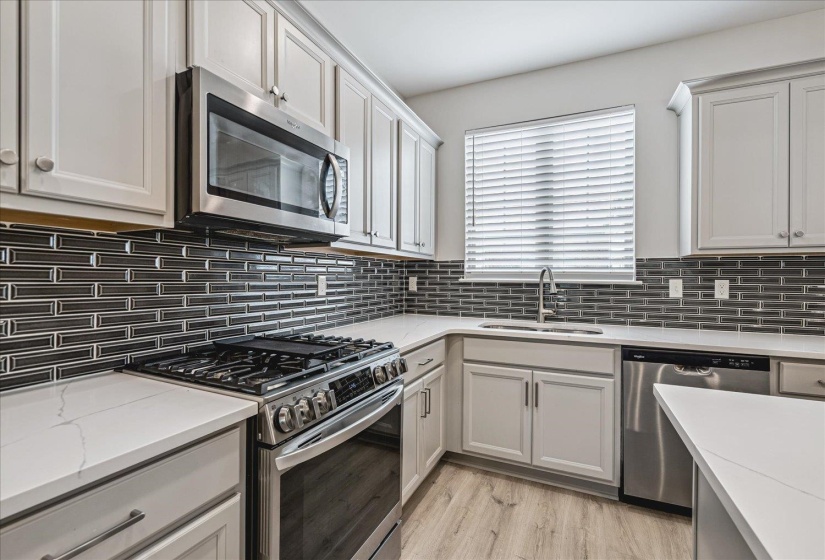 Kitchen featuring white shaker-style cabinetry, stainless steel appliances, a gray subway tile backsplash, light-toned countertops, and wood-finish flooring
