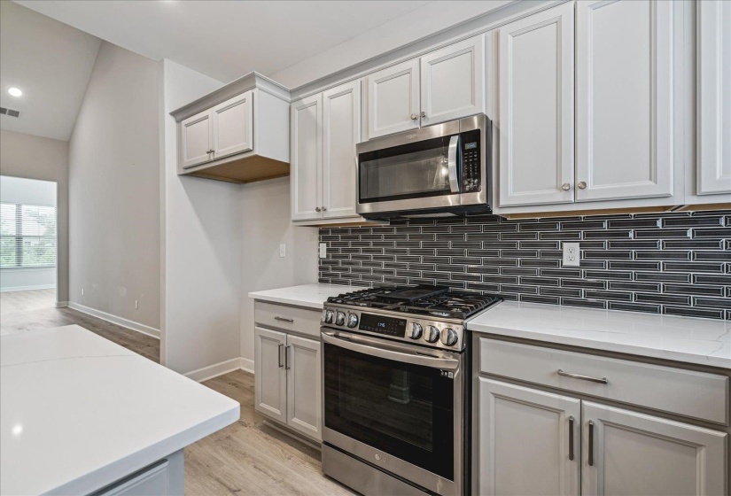 Modern kitchen featuring white shaker cabinetry, stainless steel appliances, a dark glass subway tile backsplash, and light wood-finish flooring