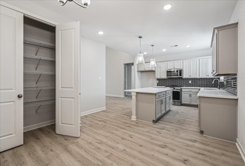 Open-concept kitchen featuring an island with pendant lighting, light wood-finish flooring, recessed lighting, white cabinetry, and a dark subway tile backsplash