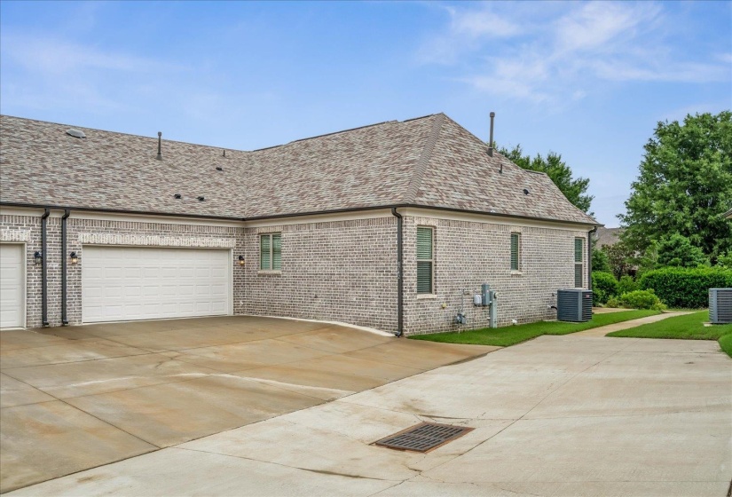 Exterior featuring light gray brickwork, a gray shingle roof, multiple windows, and a multi-car garage with white doors