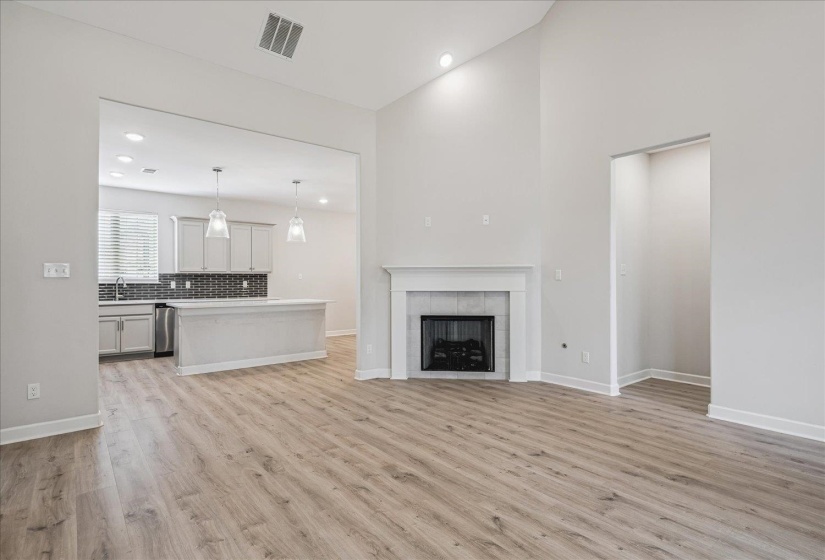 Spacious living area featuring wood-finish flooring, a fireplace with a white mantel, and high ceilings