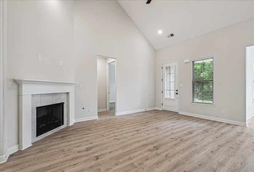 Vaulted ceiling great room with a white mantel fireplace, wood-finish flooring, and a glass-paneled exterior door