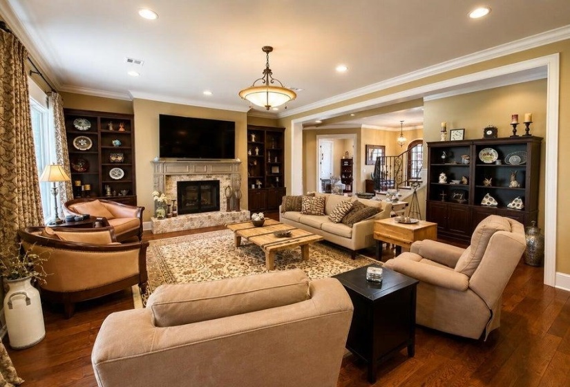 Spacious living area featuring rich wood-finish flooring, a stone-surround fireplace with a detailed mantel, and built-in cabinetry
