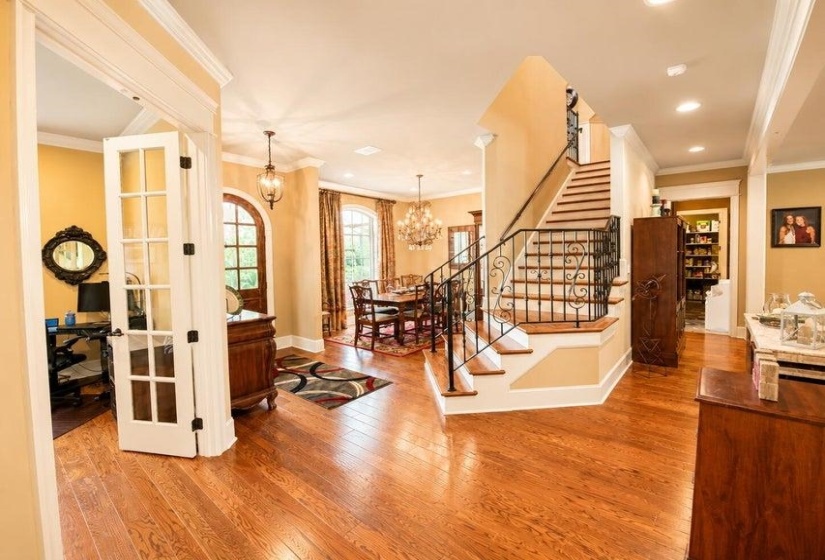 Grand foyer featuring wood-finish flooring, a staircase with wrought iron balusters, and a dining area with a chandelier