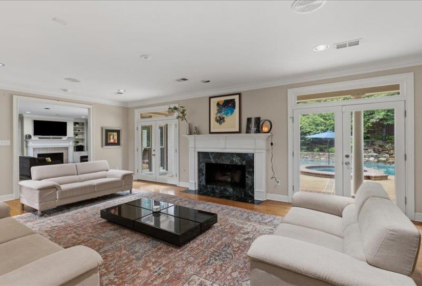 Living area featuring a white mantel fireplace with a dark stone surround and hearth, hardwood flooring, recessed lighting, and crown molding