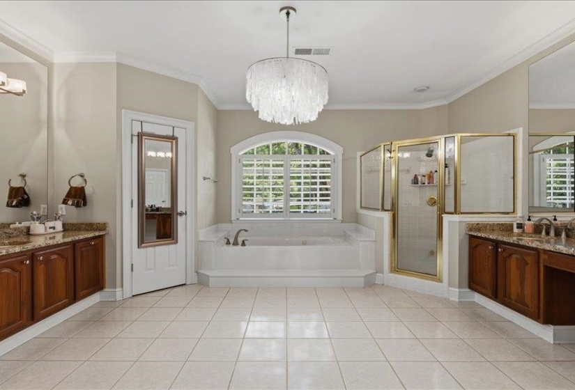 Spacious bathroom featuring a large soaking tub beneath an arched window with plantation shutters