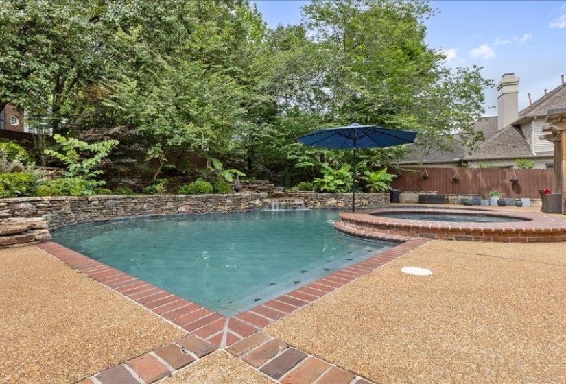 Custom-shaped swimming pool with an integrated spa, bordered by a brick coping and exposed aggregate decking