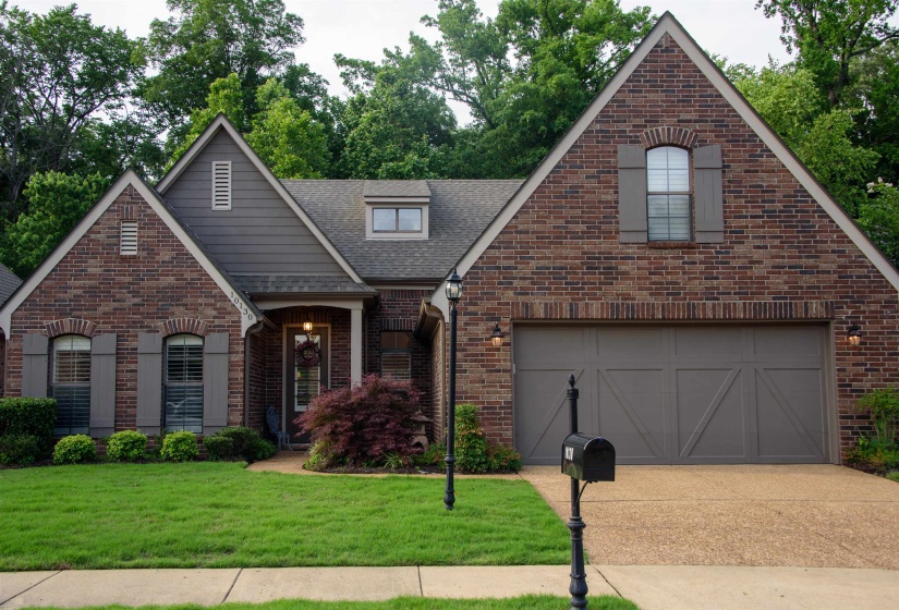 Brick facade residence featuring a front-facing attached garage, arched windows with shutters, a gabled roofline, and dormer windows