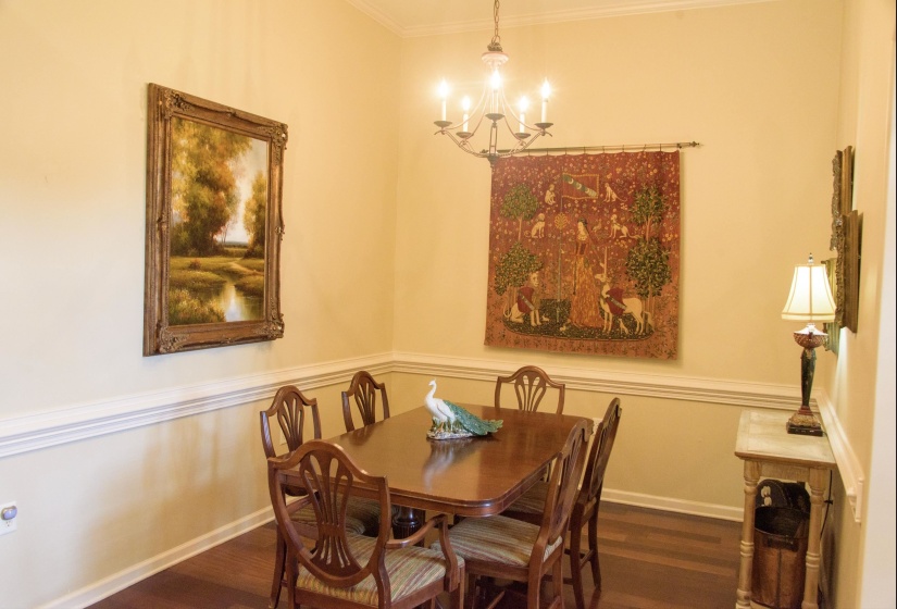 Formal dining space featuring wood-finish flooring, an overhead chandelier, crown molding, and chair rail detailing