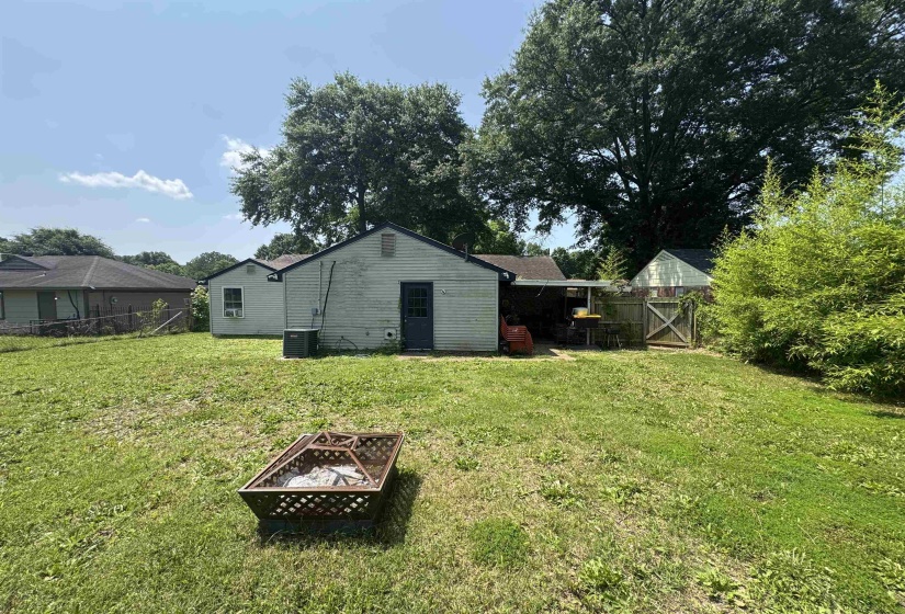 Expansive grassy backyard featuring a fire pit, mature perimeter trees, and a wooden privacy fence with a gate