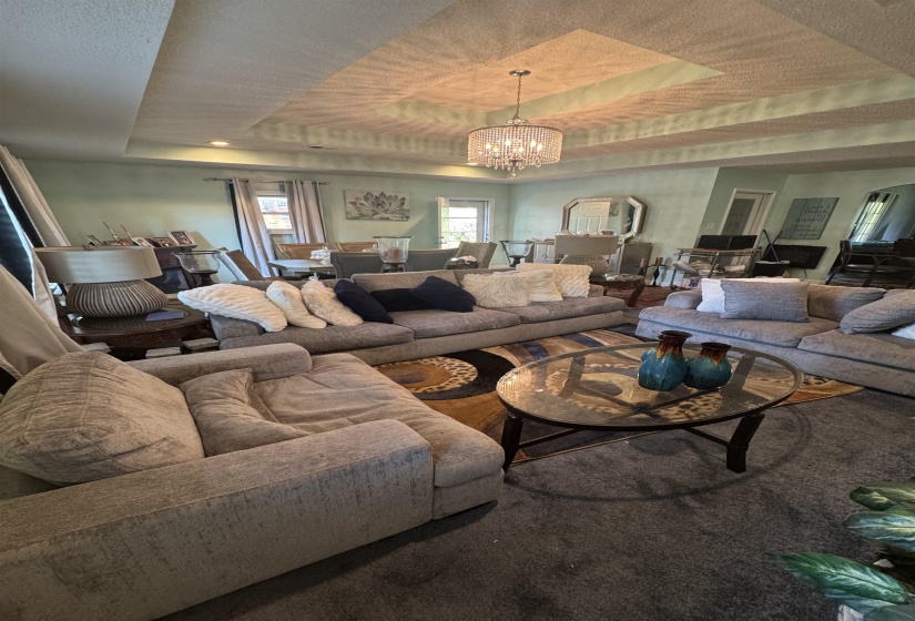 Recessed tray ceiling featuring a central chandelier, light-colored walls, and multiple windows