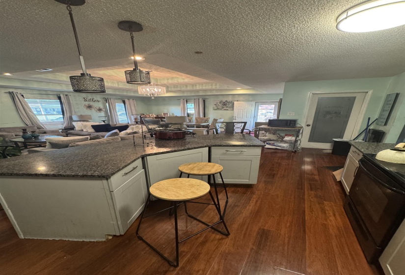 Open-concept living area featuring a kitchen island with stone countertop, wood-finish flooring, recessed lighting, and a tray ceiling