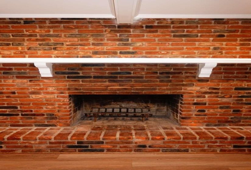 Brick fireplace featuring a hearth, white mantel, and wood-finish flooring