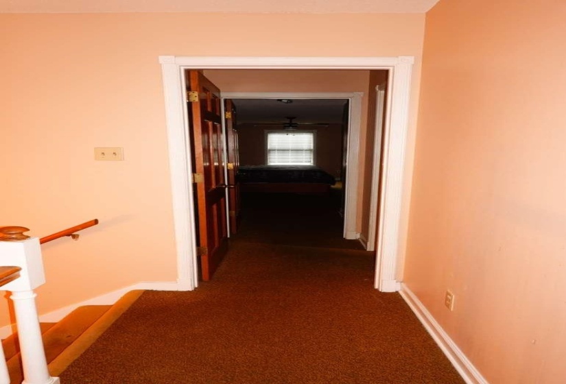 Corridor with carpeted flooring leading to a room with a ceiling fan and window