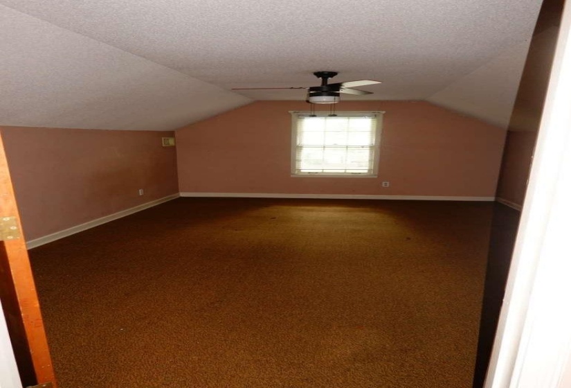Attic space featuring sloped ceilings, brown carpeting, and a window with blinds