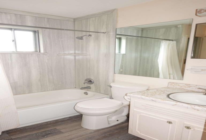 Bathroom featuring wood-finish flooring, a white vanity with a light-toned countertop, and a built-in bathtub with a window