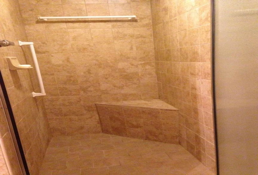Fully tiled shower enclosure featuring a built-in corner bench and integrated grab bars