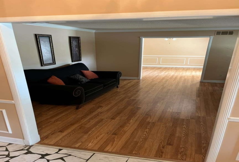 Open doorway revealing a room with wood-finish flooring, crown molding, and wainscoting