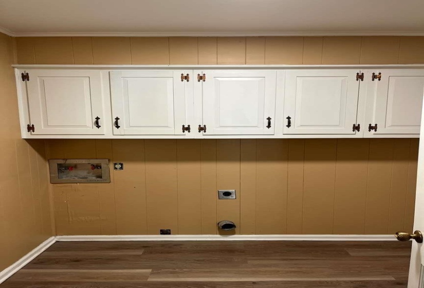 Utility area featuring wood-finish flooring, paneled wall detailing, and white upper cabinetry