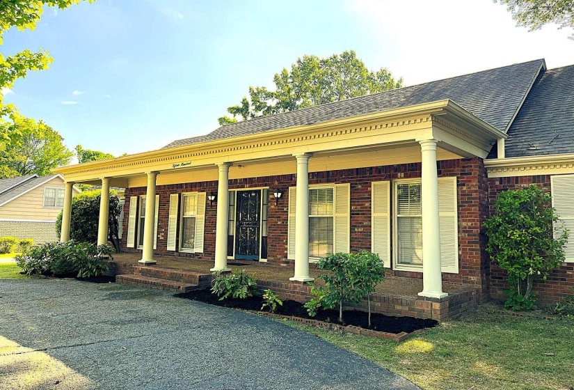 Brick facade residence featuring a covered porch with white columns, white window shutters, a dark asphalt shingle roof, and a paved driveway