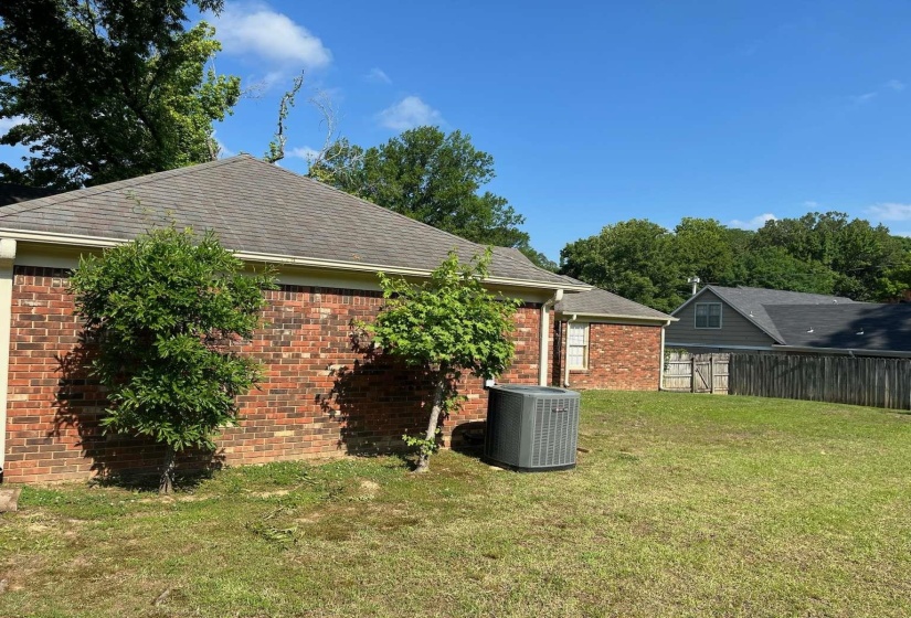Brick exterior with a gabled roofline, featuring mature landscaping, a fenced backyard, and an HVAC unit
